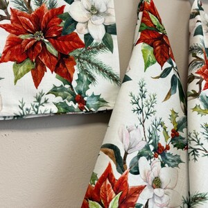 Puede incluir: Tres toallas de cocina blancas con un patr&oacute;n floral que presenta flores rojas de poinsettia, flores blancas de magnolia y bayas verdes de acebo.
