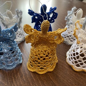 May include: Five crocheted angel ornaments in blue, gold, and white. The angels are hanging from a string and have a bell-shaped base.