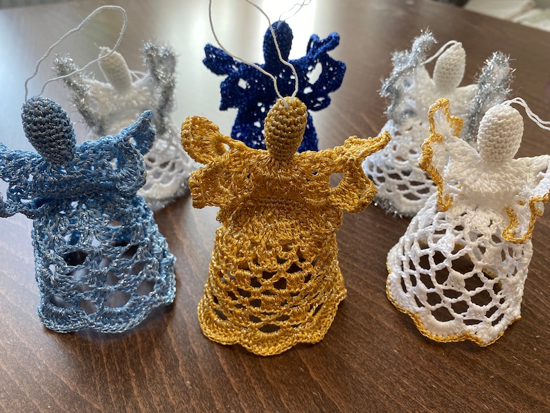 May include: Five crocheted angel ornaments in blue, gold, and white. The angels are hanging from a string and have a bell-shaped base.