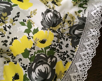 Könnte beinhalten: Weiße Tischdecke mit einem floralen Muster mit gelben, grauen und grünen Blumen. Die Tischdecke hat einen weißen Spitzenrand.