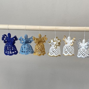 May include: Six crocheted angel ornaments hanging from a wooden dowel. The ornaments are in various colors, including blue, light blue, gold, white, and silver.