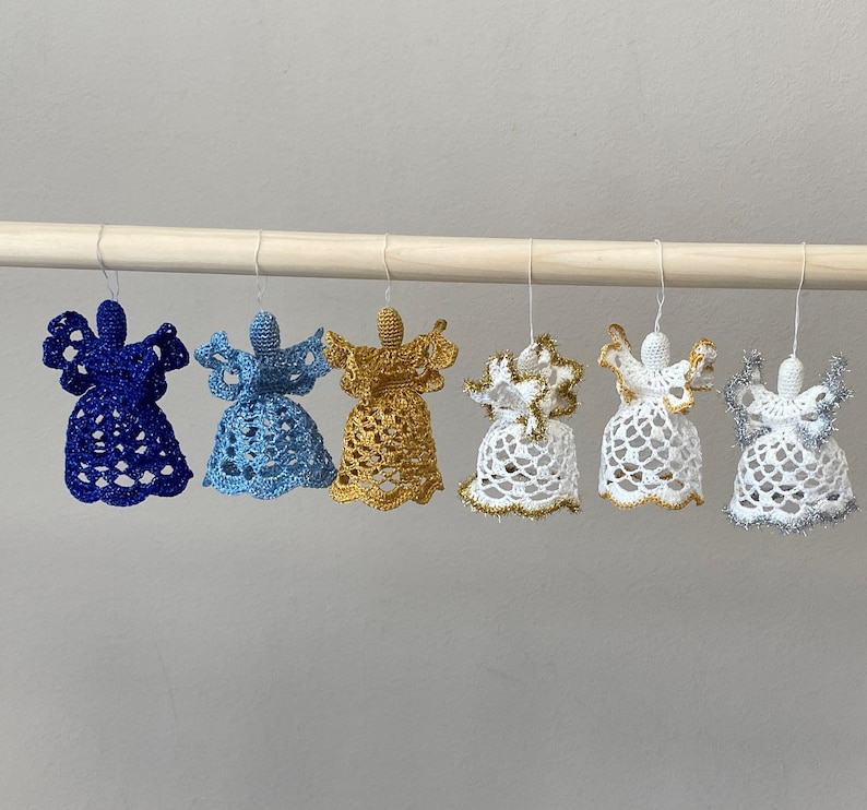 May include: Six crocheted angel ornaments hanging from a wooden dowel. The ornaments are in various colors, including blue, light blue, gold, white, and silver.