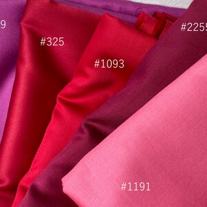 May include: Close-up of fabric swatches in shades of red and purple. The swatches are labeled with numbers: #1929, #325, #1093, #2255, and #1191. The fabrics have a smooth, satin-like texture, with varying degrees of sheen.