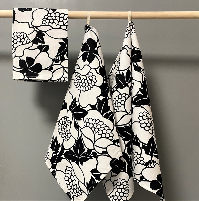 May include: Three black and white floral patterned kitchen towels hanging on a wooden rod.