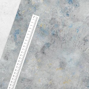 May include: A textured, abstract background in shades of gray, blue, and yellow. A white ruler with black markings and numbers from 0 to 24 centimeters is placed diagonally across the image, providing a sense of scale.