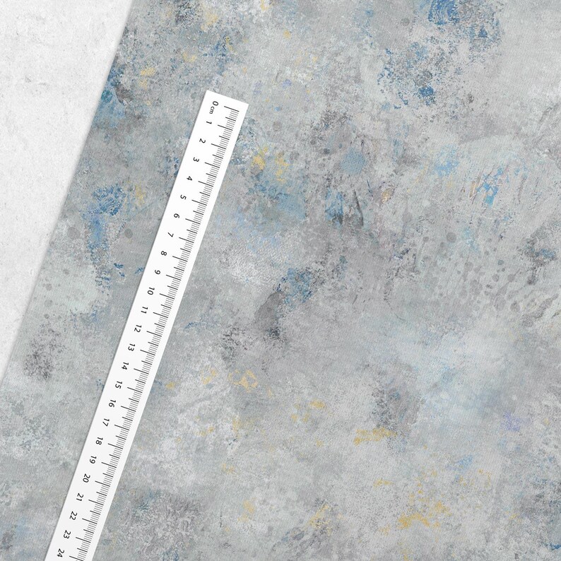 May include: A textured, abstract background in shades of gray, blue, and yellow. A white ruler with black markings and numbers from 0 to 24 centimeters is placed diagonally across the image, providing a sense of scale.