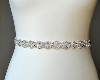 May include: A silver rhinestone belt with a delicate, intricate design. The belt is made of a thin, flexible material and is adorned with sparkling rhinestones.