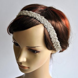 May include: A silver headband with a braided design and rhinestones. The headband is worn on a mannequin with brown hair.