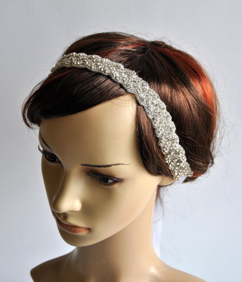 May include: A silver headband with a braided design and rhinestones. The headband is worn on a mannequin with brown hair.