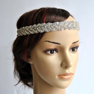 May include: A silver headband with a braided design and rhinestones. The headband is worn on a mannequin with brown hair.