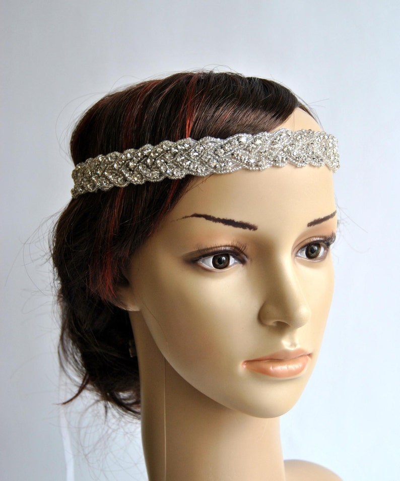 May include: A silver headband with a braided design and rhinestones. The headband is worn on a mannequin with brown hair.