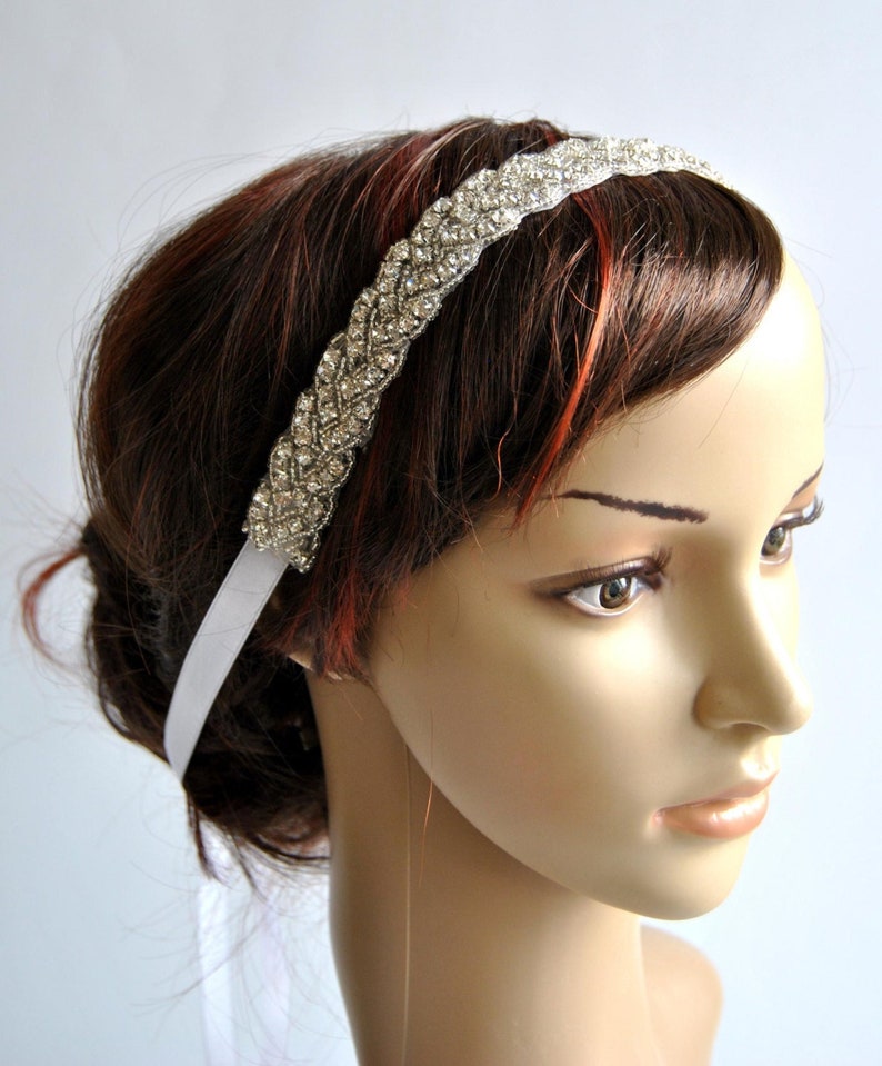 May include: A white satin headband with a braided design embellished with clear rhinestones.
