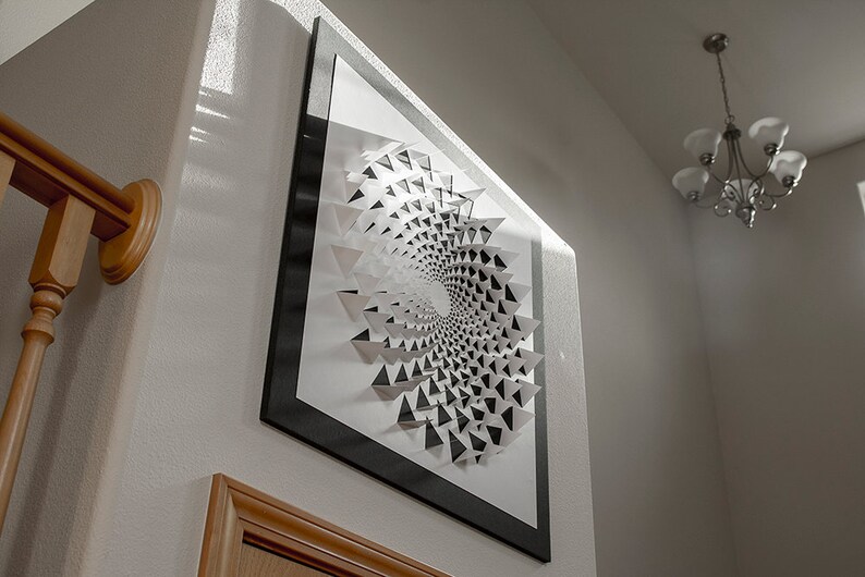 May include: A black and white geometric art print in a black frame. The print features a spiral design made of triangles.