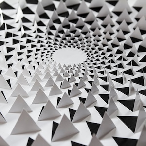 Puede incluir: Una pieza de arte en papel en blanco y negro con un patrón en espiral de triángulos. Los triángulos están dispuestos en un círculo, creando una sensación de profundidad y dimensión.