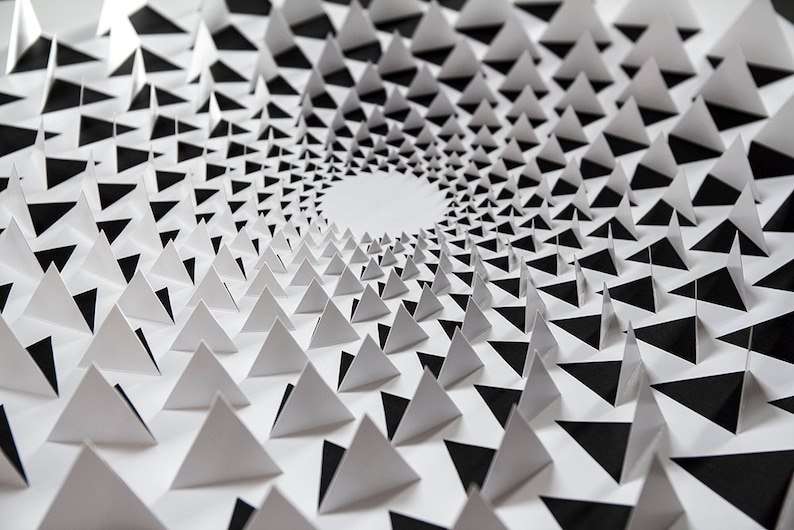 May include: A black and white paper art piece with a spiral pattern of triangles. The triangles are arranged in a circle, creating a sense of depth and dimension.