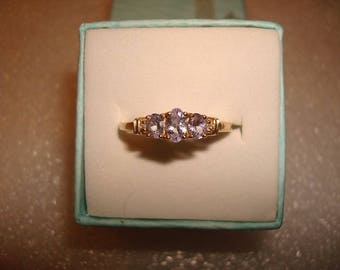 May include: A gold ring with three oval-shaped light purple gemstones set in a row.
