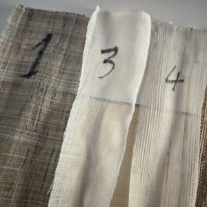 May include: Close-up of four different fabric swatches. The swatches are numbered 1, 3, and 4 in black ink. The fabrics vary in color and texture, ranging from a coarse, woven material to a smooth, light-colored fabric.