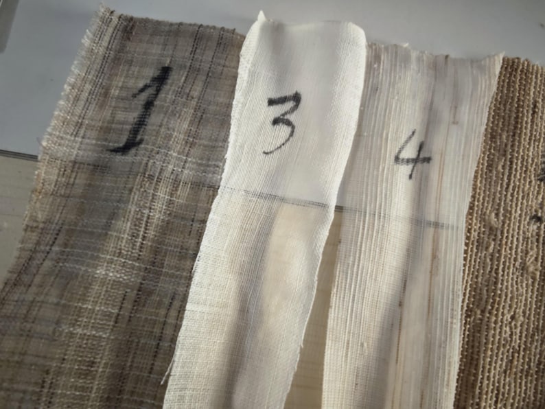 May include: Close-up of four different fabric swatches. The swatches are numbered 1, 3, and 4 in black ink. The fabrics vary in color and texture, ranging from a coarse, woven material to a smooth, light-colored fabric.