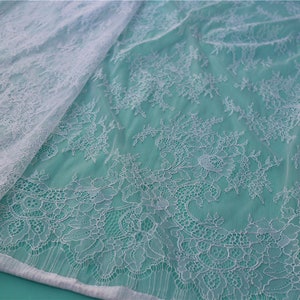 May include: White lace fabric with a delicate floral pattern. The lace is sheer and has a soft, flowing texture.