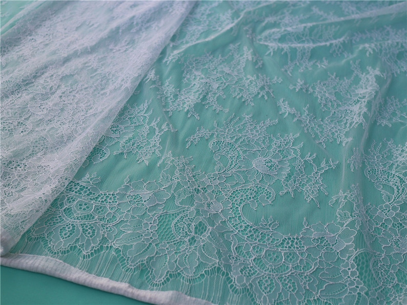 May include: White lace fabric with a delicate floral pattern. The lace is sheer and has a soft, flowing texture.