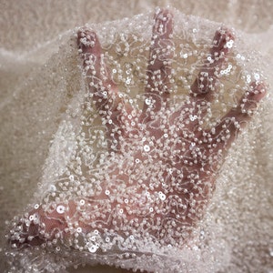 May include: White beaded fabric with a delicate floral pattern. The fabric is sheer and has a subtle sparkle.