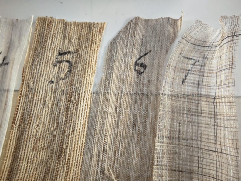 May include: Close-up of several fabric swatches with varying textures and colors, including beige, tan, and off-white. Each swatch is labeled with a number in black ink. The fabrics appear to be natural fibers.