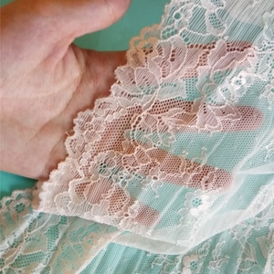 Puede incluir: Tela de encaje blanca con un delicado patrón floral. El encaje es suave y transparente, con una textura delicada.