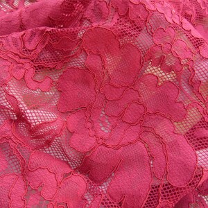 May include: Close-up of a red lace fabric with a floral pattern. The lace is delicate and intricate, with a fine mesh background.