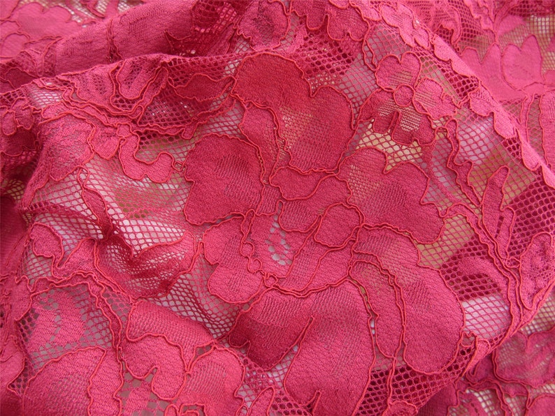 May include: Close-up of a red lace fabric with a floral pattern. The lace is delicate and intricate, with a fine mesh background.
