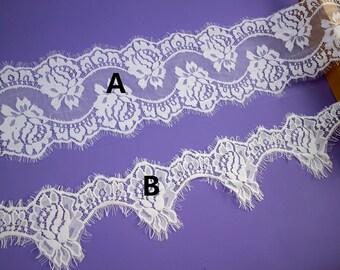 May include: Two white lace trims with scalloped edges. Trim A has a larger floral pattern than trim B. Both trims have a frayed edge.