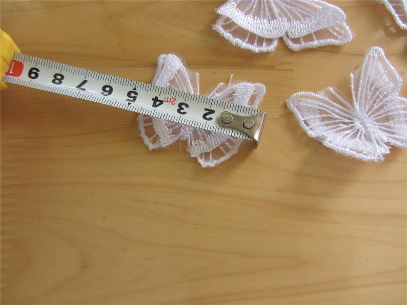 May include: White lace butterfly appliques with a measuring tape showing 3 inches. These delicate appliques are perfect for adding a touch of elegance to any project.