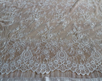 May include: White lace fabric with a delicate floral pattern. The lace has a scalloped edge and is sheer.