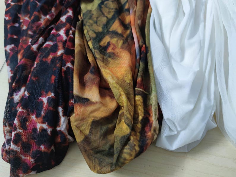 Peut inclure: Gros plan sur trois tissus diff&eacute;rents. L'un est un imprim&eacute; animalier rouge fonc&eacute; et noir, le second un motif abstrait marron et jaune, et le troisi&egrave;me un tissu blanc transparent. Les tissus sont drap&eacute;s et pli&eacute;s.