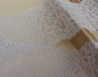 May include: White lace trim with a delicate floral pattern. The lace is soft and sheer, with a scalloped edge.