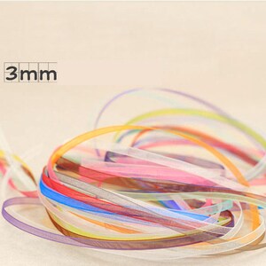 May include: A pile of colorful 3mm wide sheer ribbon. The ribbon is in a variety of colors, including pink, blue, yellow, and green.