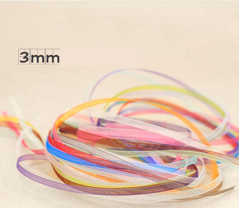 May include: A pile of colorful 3mm wide sheer ribbon. The ribbon is in a variety of colors, including pink, blue, yellow, and green.