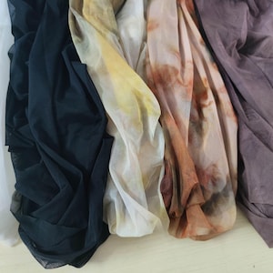 Peut inclure: Collection de tissus drap&eacute;s de diff&eacute;rentes couleurs. Les tissus comprennent du blanc, du noir, du jaune et des nuances de marron et de violet. Les mati&egrave;res semblent l&eacute;g&egrave;res et transparentes, certaines pr&eacute;sentant un motif aquarelle.