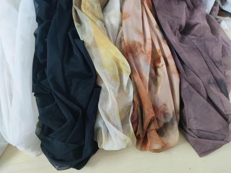 Peut inclure: Collection de tissus drap&eacute;s de diff&eacute;rentes couleurs. Les tissus comprennent du blanc, du noir, du jaune et des nuances de marron et de violet. Les mati&egrave;res semblent l&eacute;g&egrave;res et transparentes, certaines pr&eacute;sentant un motif aquarelle.
