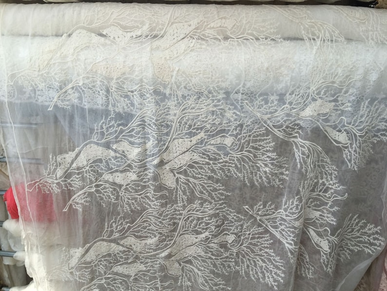 Puede incluir: Tela blanca transparente con un delicado patr&oacute;n floral blanco. La tela tiene una textura suave y fluida, ideal para crear prendas de vestir, decoraci&oacute;n del hogar o accesorios.