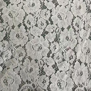 May include: A white lace fabric featuring a repeating floral pattern with intricate petal details and scalloped edges. The delicate textile displays a complex network of interconnected threads forming large blossoms across the entire surface area.