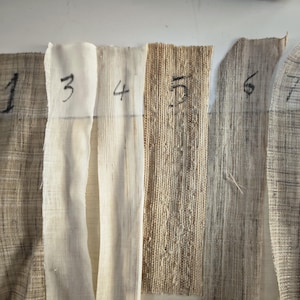 May include: A collection of seven fabric swatches in varying shades of beige and brown. Each swatch is numbered with black marker from 1 to 7. The fabrics have different textures, ranging from tightly woven to loosely woven, and some are semi-transparent.