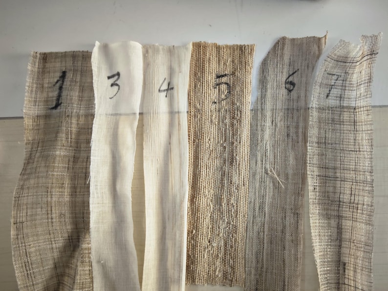 May include: A collection of seven fabric swatches in varying shades of beige and brown. Each swatch is numbered with black marker from 1 to 7. The fabrics have different textures, ranging from tightly woven to loosely woven, and some are semi-transparent.