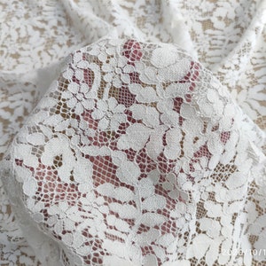 May include: White lace fabric with a delicate floral pattern. The lace is soft and sheer, and it would be perfect for a variety of projects, such as wedding dresses, tablecloths, and curtains.