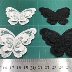 May include: Four butterfly-shaped lace appliques, two white and two black, on a green cutting mat. The appliques are layered and have a delicate, intricate design.