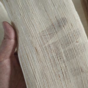 May include: Close-up of a cream-colored, loosely woven fabric. The fabric has a textured appearance with visible threads and small imperfections. The weave is open, allowing some light to pass through. The fabric is being held.