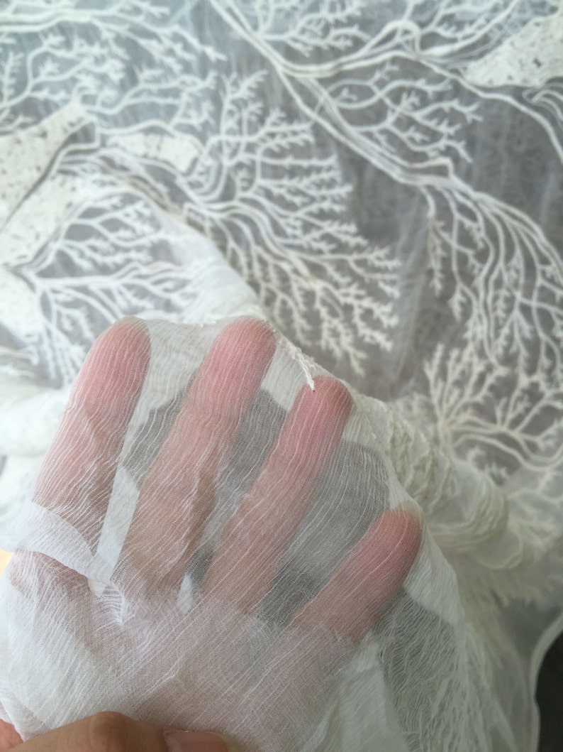 Puede incluir: Tela blanca transparente con un dise&ntilde;o de &aacute;rbol bordado. La tela es delicada y tiene una textura suave y fluida.