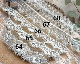 May include: Five different white lace trims with scalloped edges and fringe. The trims are labeled with numbers 64, 65, 66, 67, and 68.