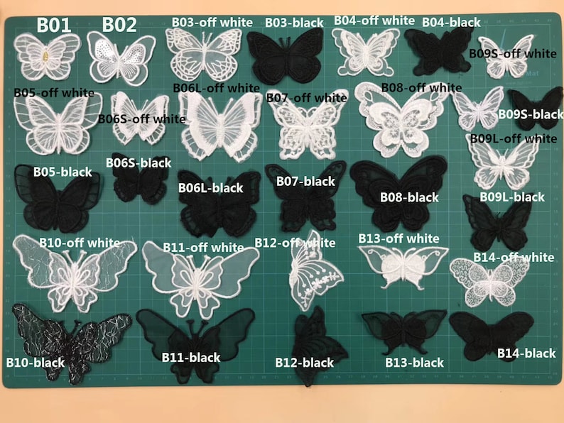 May include: A collection of 14 black and white butterfly appliques. The appliques are arranged in rows on a green cutting mat. Each applique is labeled with a letter and color combination, such as B01, B02, B03-off white, B03-black, etc.