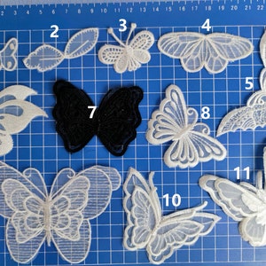 May include: Assortment of 11 white and black lace butterfly appliques. The appliques are arranged on a blue grid background. The appliques are numbered 1 through 11.