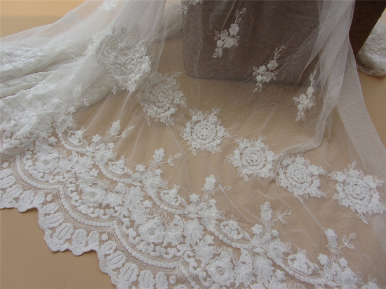 Pu&ograve; includere: Tessuto di tulle bianco ricamato con un delicato motivo floreale. Il tessuto ha una texture morbida e fluida, perfetto per progetti di artigianato e cucito.